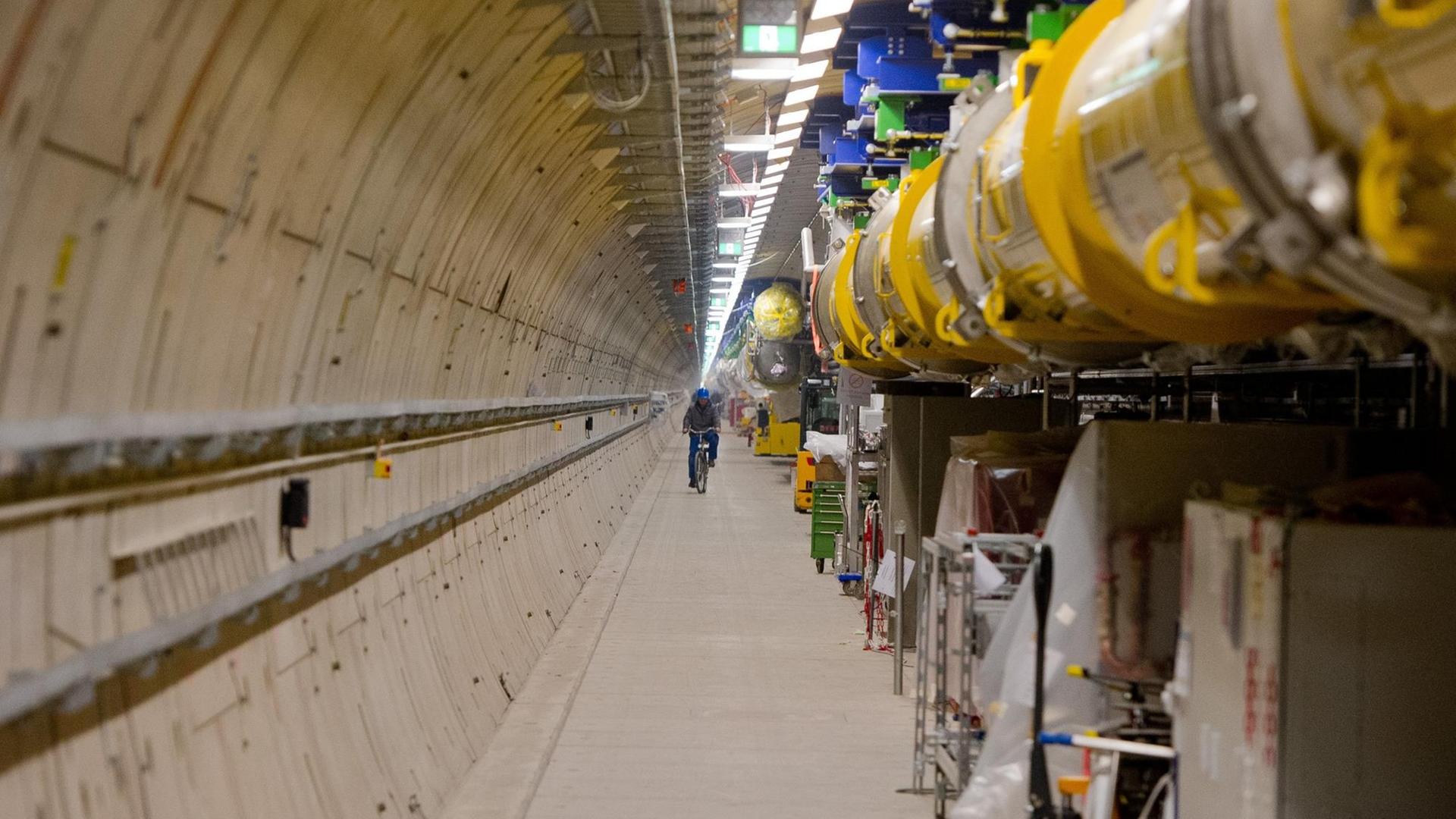 Ein Mitarbeiter fährt am 18.02.2015 in Hamburg im Teilchenbeschleuniger-Tunnel des Röntgenlaser-Projekts European XFEL mit einem Fahrrad am Beschleuniger (gelb) entlang. Das Projekt umfasst eine 3,4 Kilometer lange Tunnelanlage.