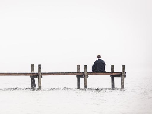 Ein Mann sitz einsam an einem Bootssteg.