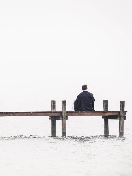 Ein Mann sitz einsam an einem Bootssteg.