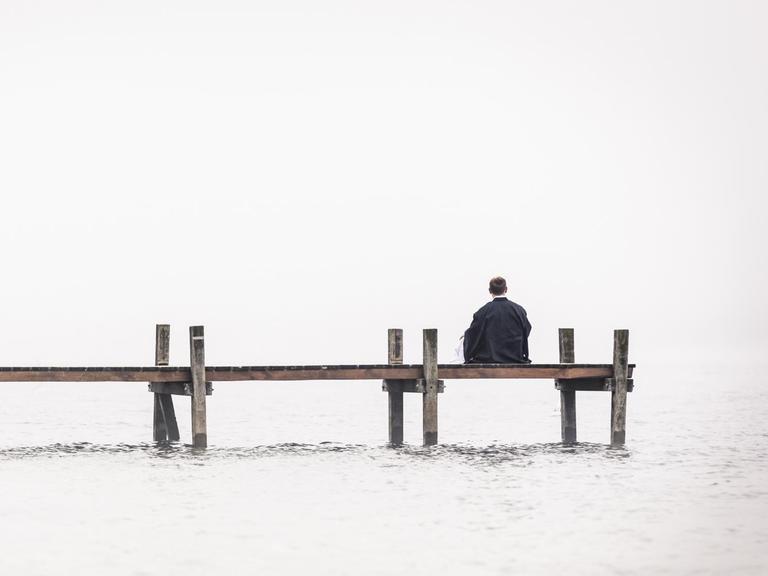 Ein Mann sitz einsam an einem Bootssteg.