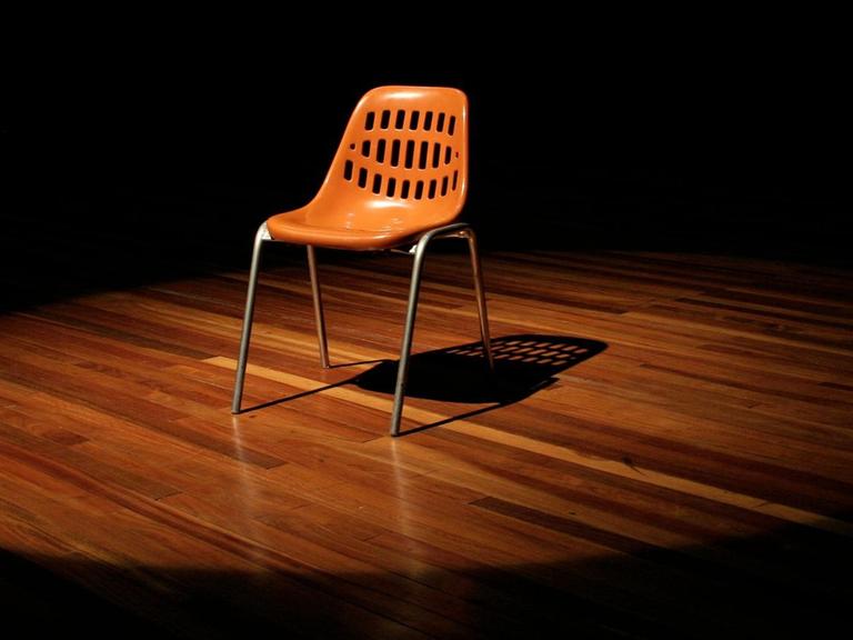 Ein leerer Stuhl steht auf einer Theaterbühne.