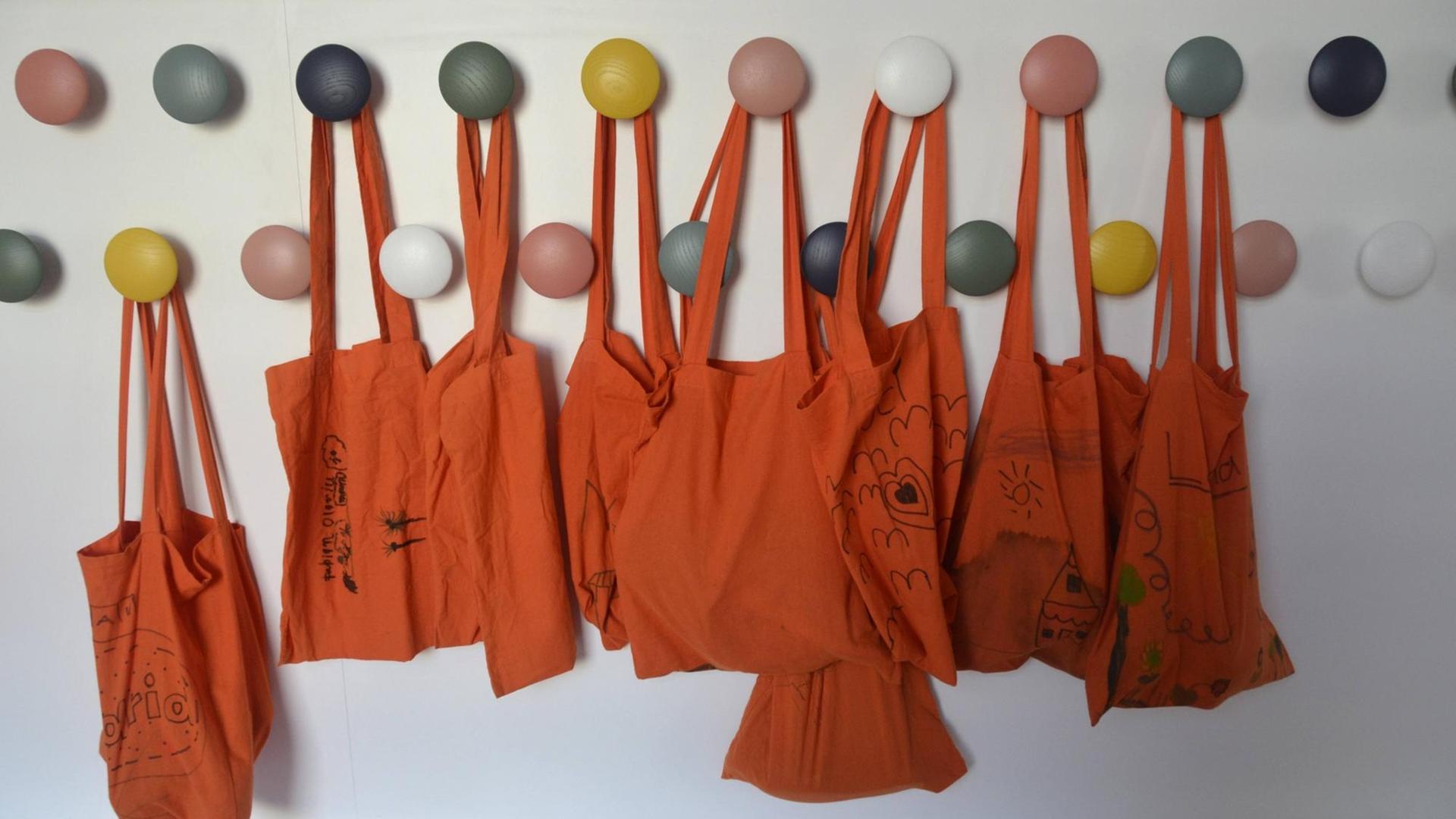 An bunten Haken hängen orangefarbene Stoffbeutel.
