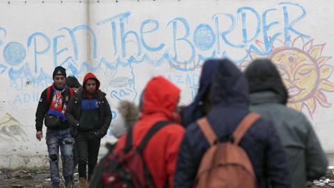 Flüchtlinge stehen am 18.12.2017 in Sid (Serbien), nahe der Grenze zu Kroatien vor einer Mauer mit der Aufschrift "Öffnet die Grenze".