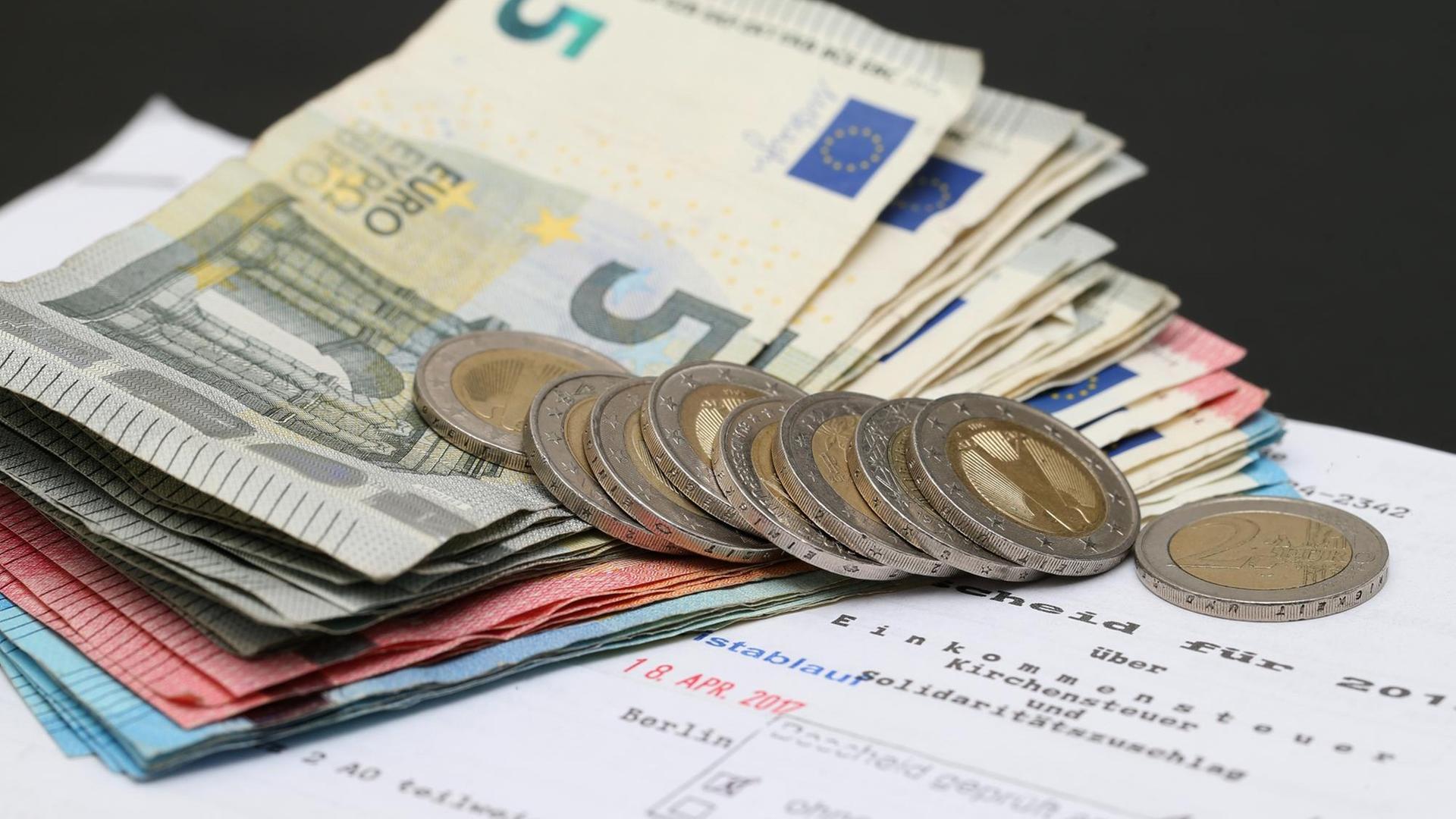 Symbolbild Steuererklärung, Steuerbescheid mit Euro-Münzen und -Scheinen