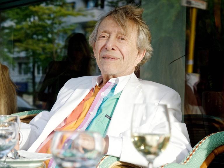 Rolf Eden sitzt an einem Caféhaustisch vor der Paris Bar in Berlin und isst Mittag.