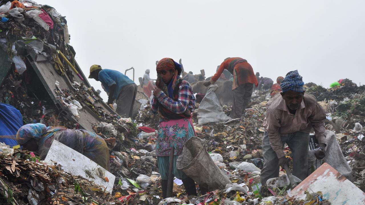 Abfälle werden auf einen Müllberg vor Delhi bebracht - und Menschen suchen nach Wertvollem.