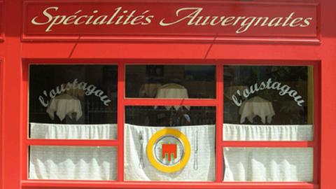 Französisches Restaurant in der Auvergne: Rote Fassade, weiße Vorhänge in den Fenstern.