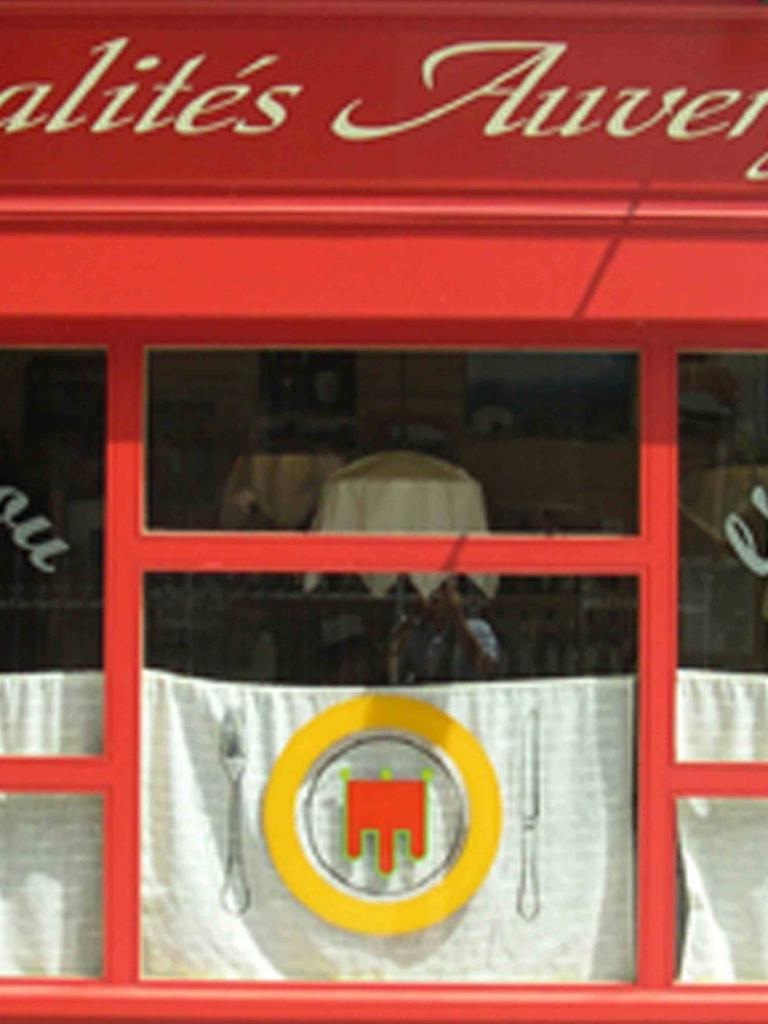 Französisches Restaurant in der Auvergne: Rote Fassade, weiße Vorhänge in den Fenstern.