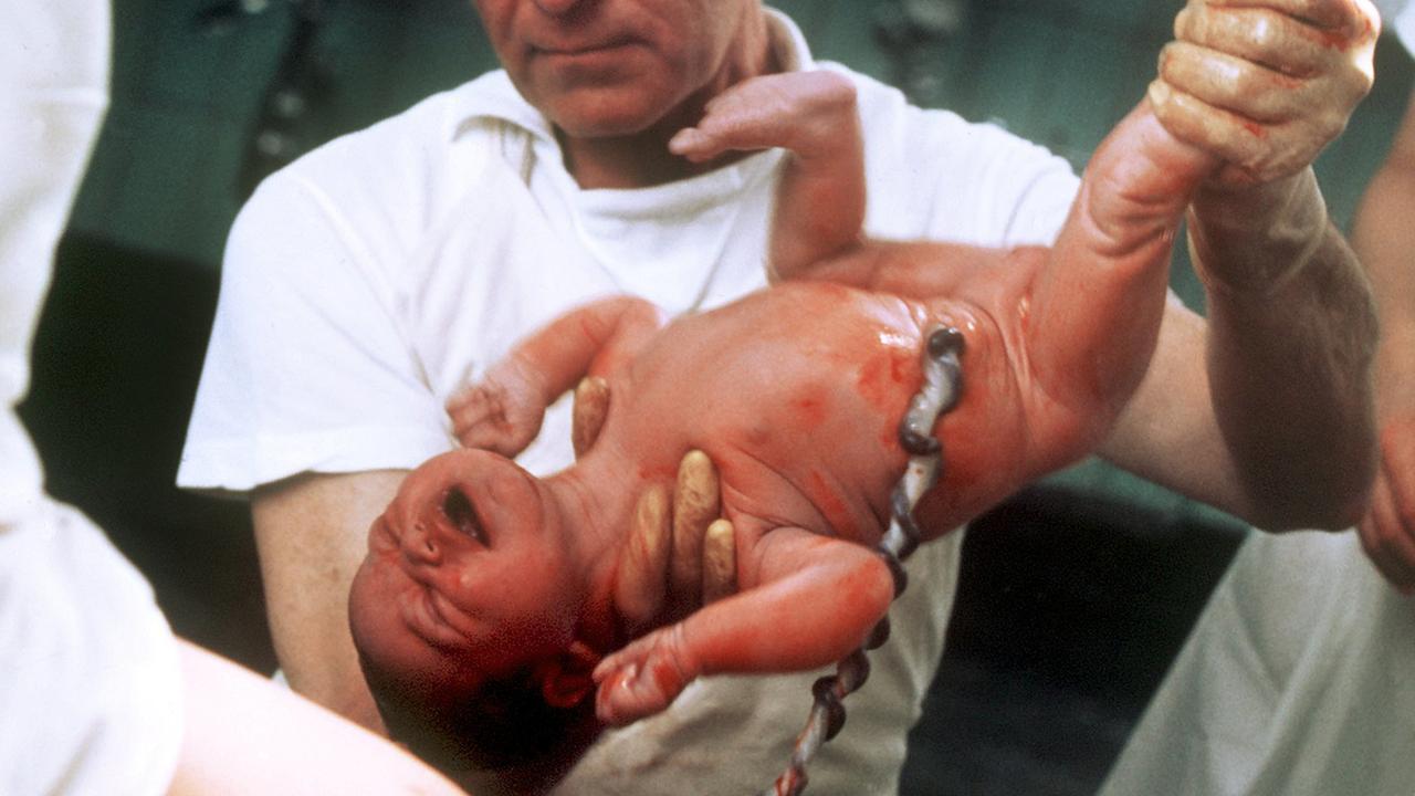 Ein Arzt im Kreißsaal hält einen neugeborenen Säugling hoch.