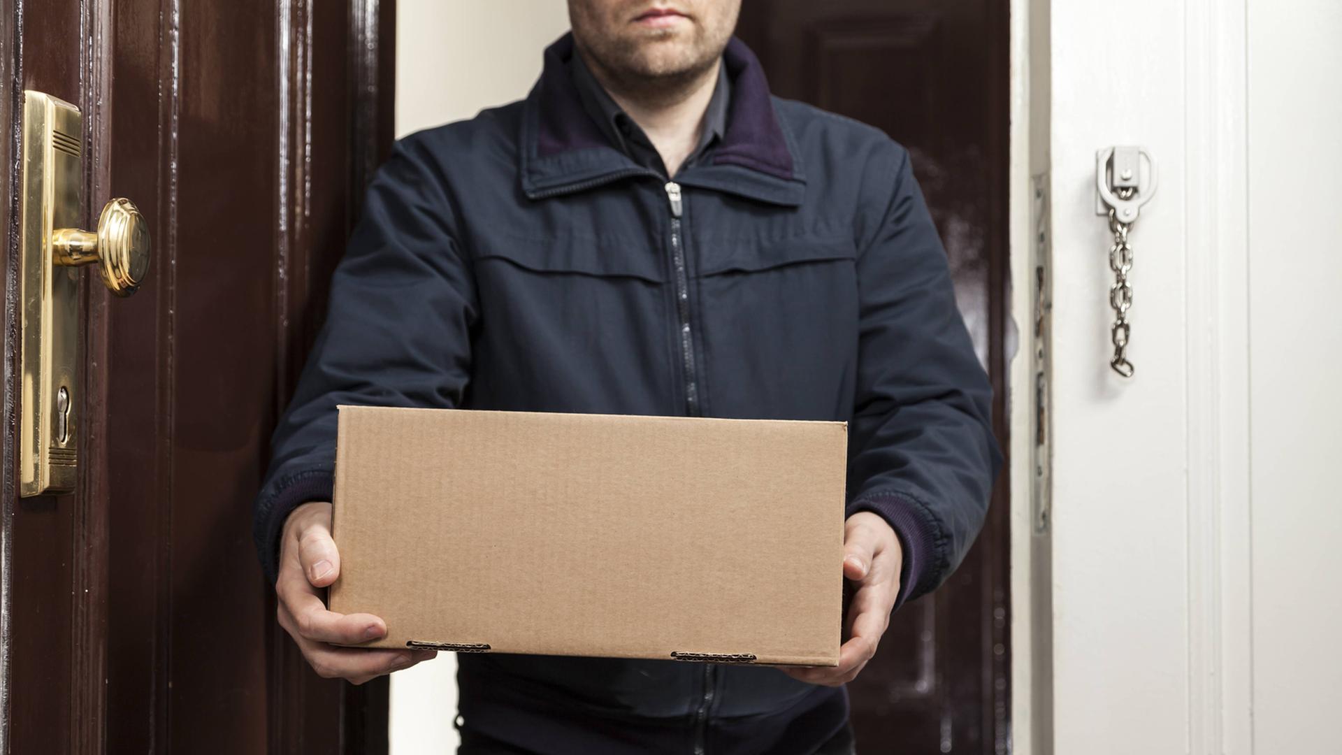 Ein Postbote bringt ein Paket an die Haustüre.