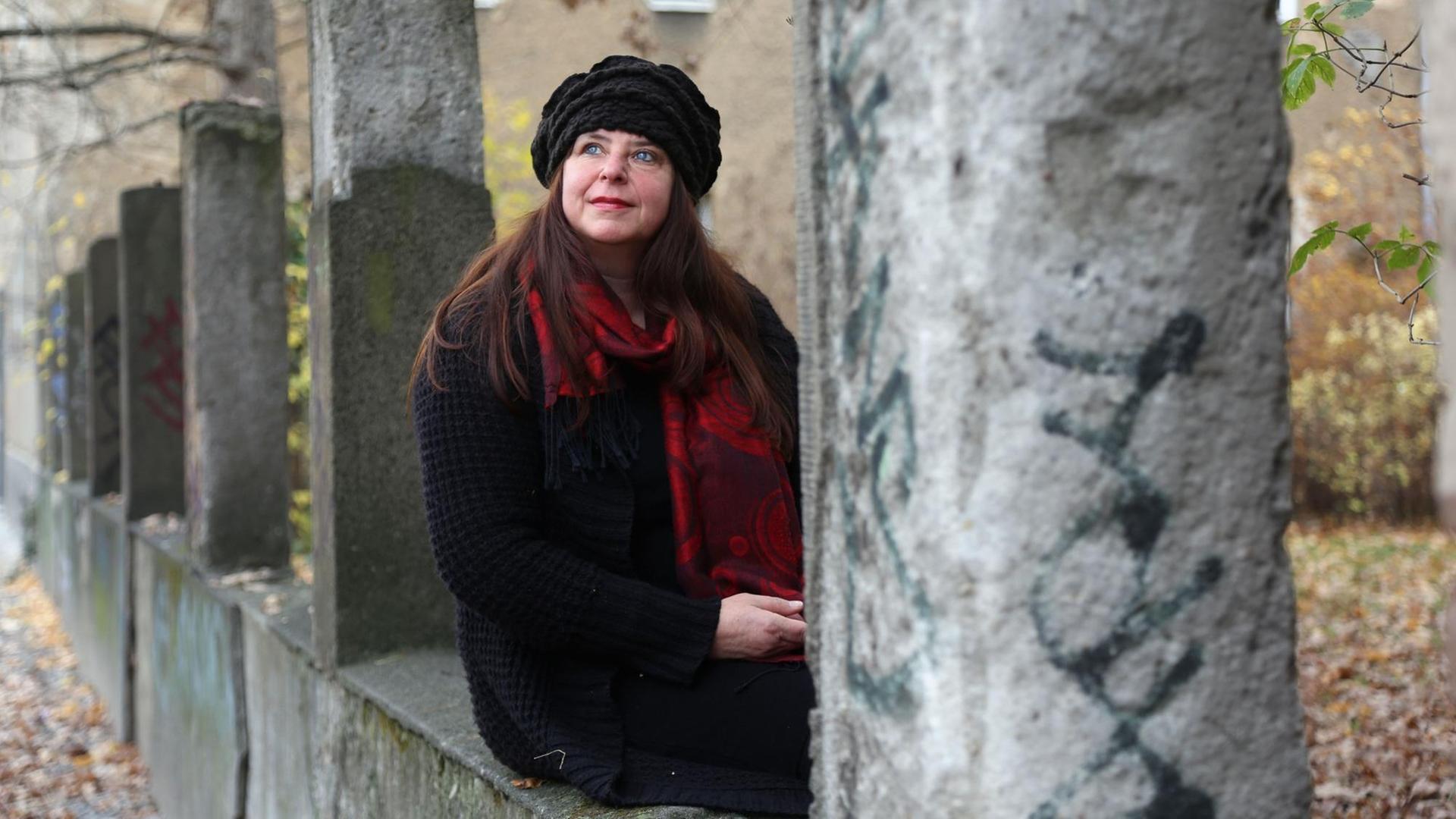 Annett Gröschner sitzt auf einer Mauer zwischen Säulen und herbstlichem Laub.
