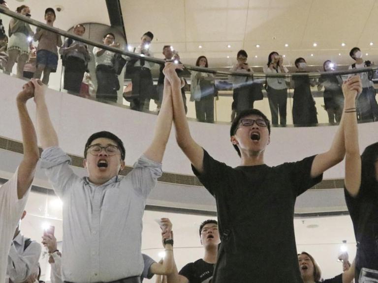 Demonstranten singen 2019 in einem Einkaufszentrum "Glory To Hongkong" und halten sich an den Händen.
