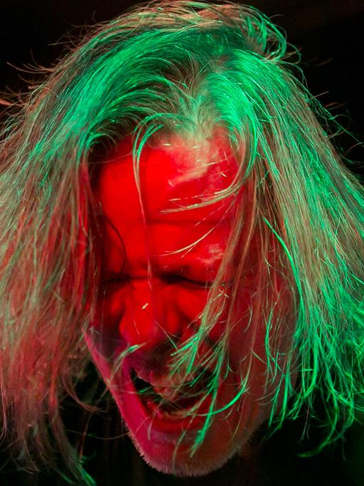 Gitarrist und Sänger Michael Gira der amrerikanischen Post-Punk-Band Swans bei einem Auftritt 2013 im Akvarium Klub in Budapest. Sein Kopf ist grün-rot angestrahlt, das Haar zerzaust, das Gesicht zum Schrei verzerrt.