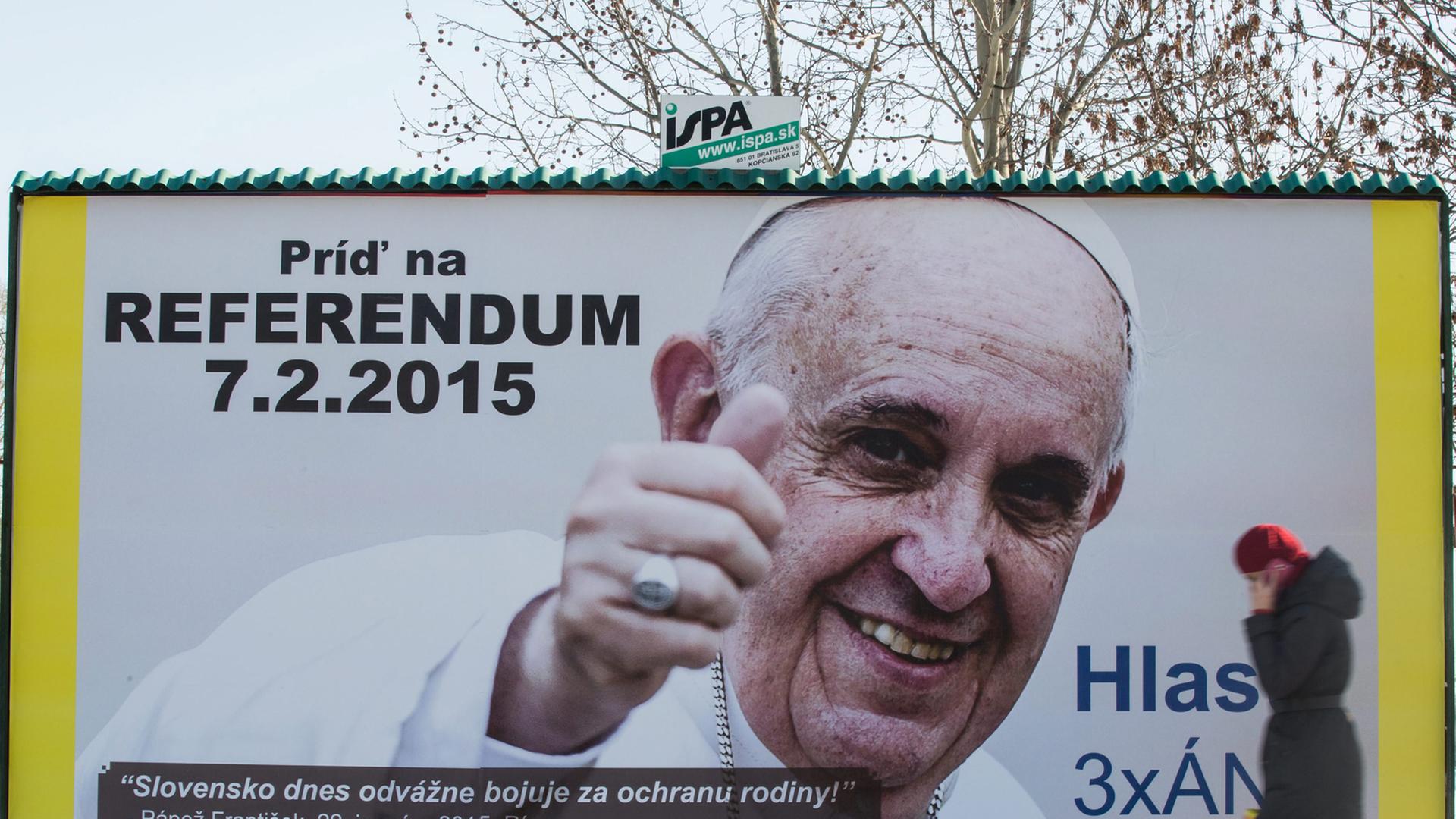 Werbeplakat für das Referendum mit Bild und Zitat von Papst Franziskus, davor geht eine Frau vorbei.