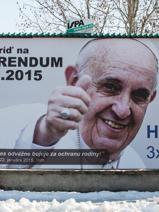 Werbeplakat für das Referendum mit Bild und Zitat von Papst Franziskus, davor geht eine Frau vorbei.