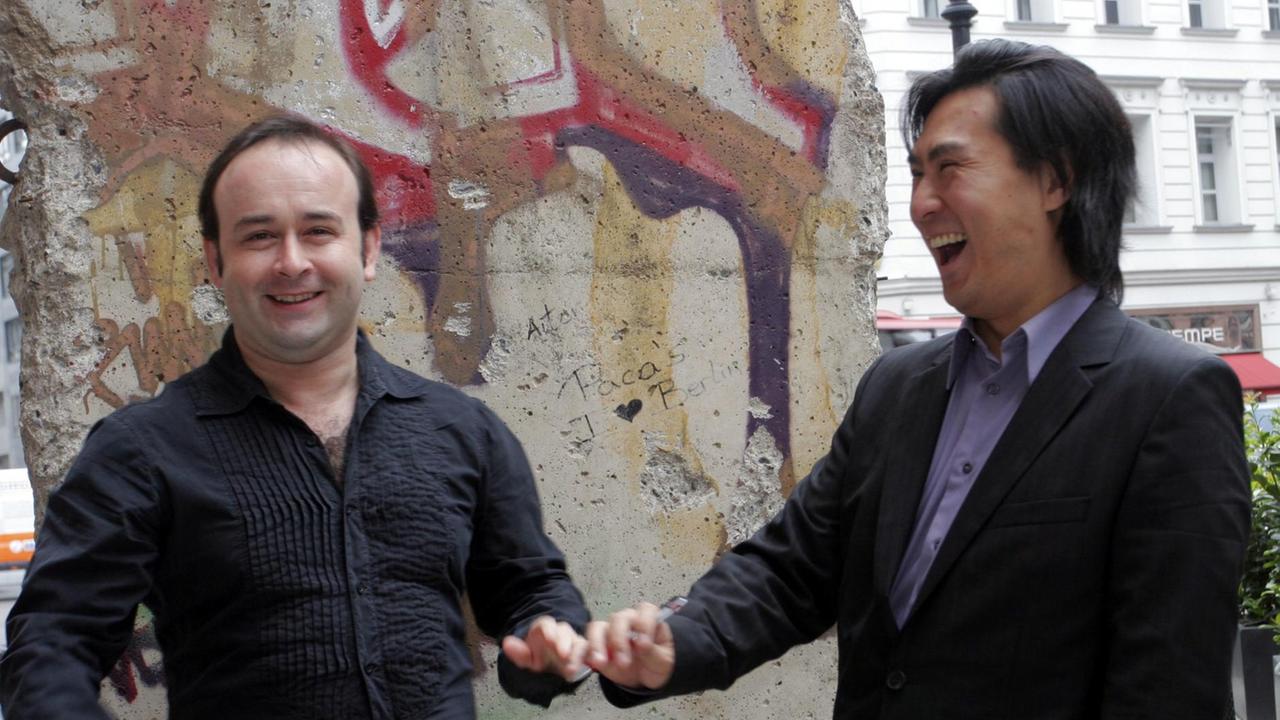 Die Musiker Aleksey Igudesman (l., Geige) und Richard Hyung-ki Joo (Piano) scherzen am Mittwoch (02.06.2010) bei einem Pressetermin in Berlin vor einem Mauerteil.