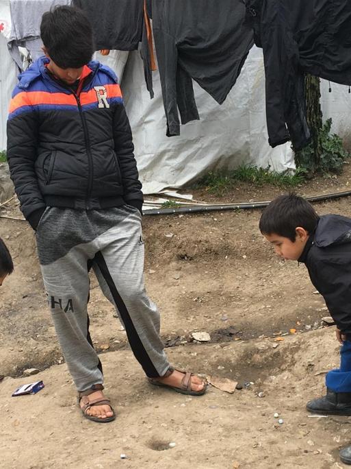 Kinder spielen, in einen sorglosen Moment, mit Murmeln in einem Flüchtlingslager auf Lesbos.
