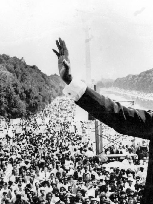 Martin Luther King steht in Washington vor einer Menschenmenge und winkt, im Hintergrund das Lincoln Memorial. Aufnahme vom 30. August 1963.