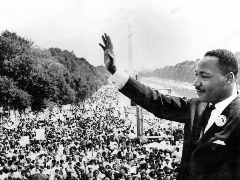 Martin Luther King steht vor einer großen Menschenmenge und winkt. 