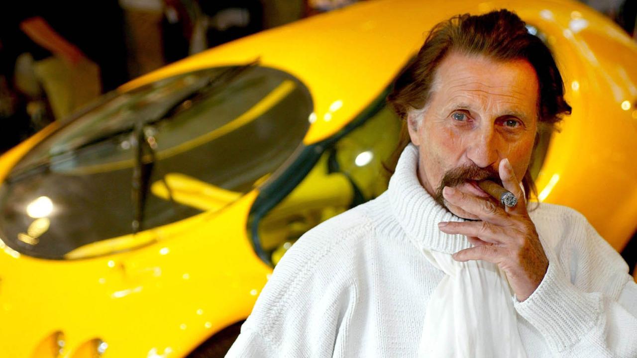Das Bild zeigt den Designer Luigi Colani mit einer Zigarre im Mund vor einem knallgelben Auto.