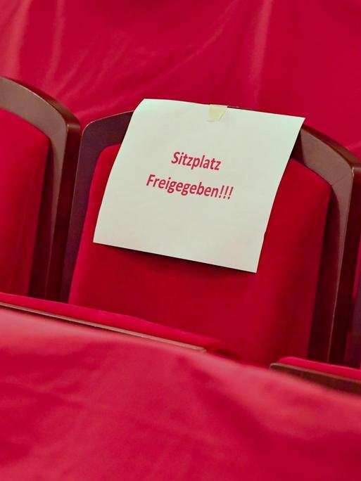 Ein Schild mit der Aufschrift "Sitzplatz freigegeben!!!" liegt auf einem roten Theatersitz.