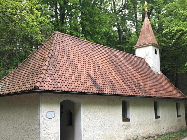 Die St. Corona-Kapelle im bayerischen Sauerlach-Arget: Eine schlichte, weiß verputzte Kapelle mit rotem Ziegeldach und einem kleinen Turm steht im Wald