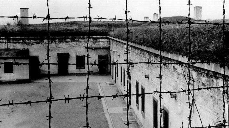 Blick durch Stacheldraht auf die Gebäude des 1941 von der SS errichteten Konzentrationslagers im tschechischen Theresienstadt.