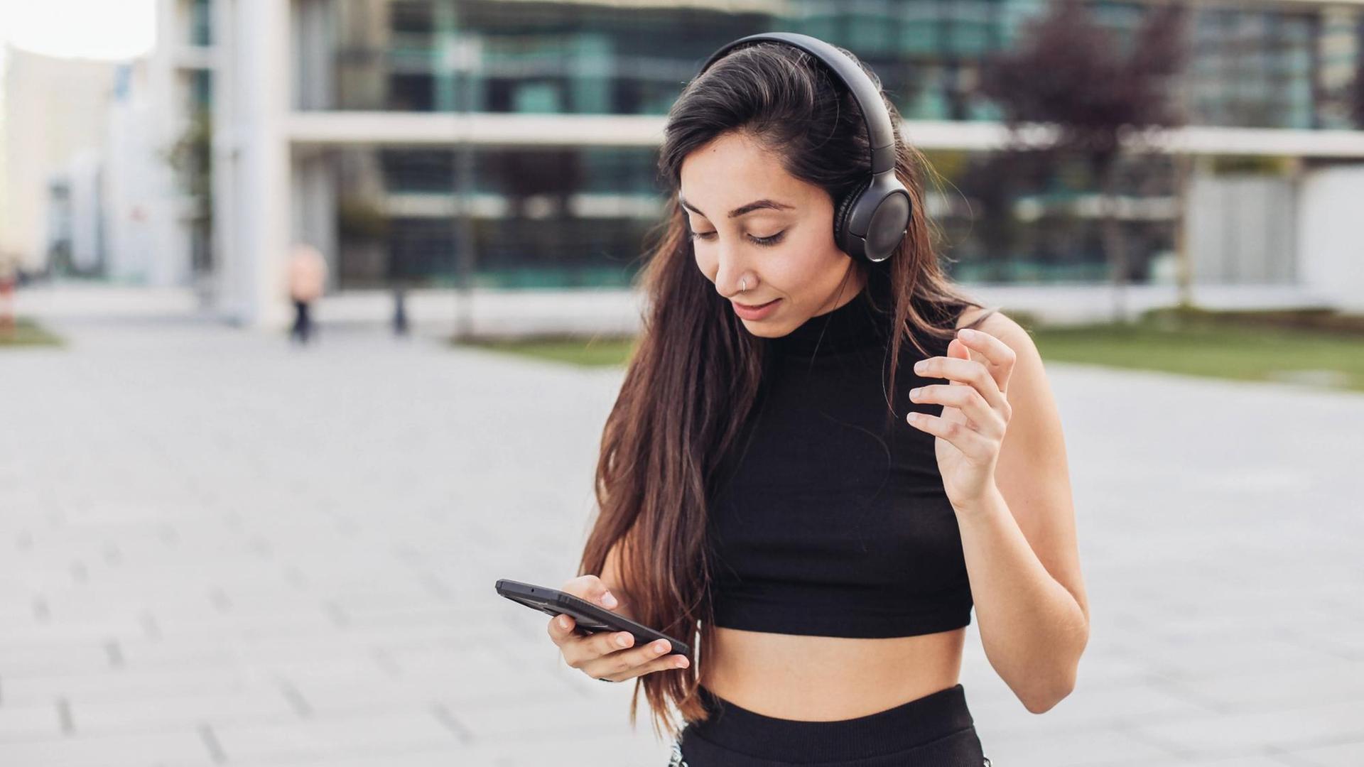 Junge Frau mit Kopfhörern schaut auf ihr Smartphone