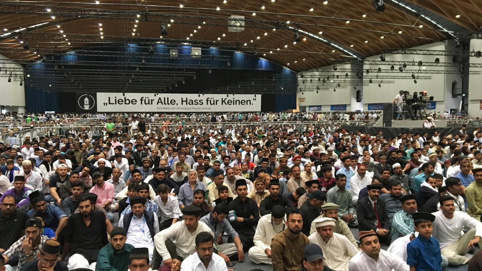 Muslime sitzen am 25.08.2017 auf der Jahreshauptversammlung der muslimischen Bewegung Ahmadiyya Muslim Jamaat in Rheinstetten (Baden-Württemberg) in einer Halle und hören einer Predigt zu.
