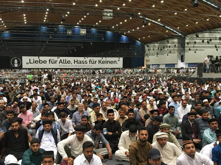Muslime sitzen am 25.08.2017 auf der Jahreshauptversammlung der muslimischen Bewegung Ahmadiyya Muslim Jamaat in Rheinstetten (Baden-Württemberg) in einer Halle und hören einer Predigt zu.