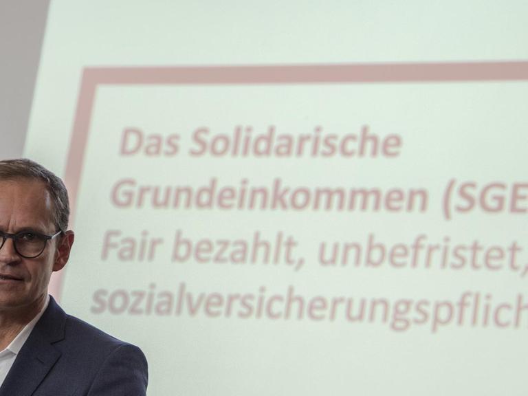 Der Regierende Bürgermeister Michael Müller (SPD) vor einer Wand, auf die mit einem Beamer die Schrift projiziert ist "Das Solidarische Grundeinkommen (SGE): fair bezahlt, frei[willig], sozialversicherungspflichtig"