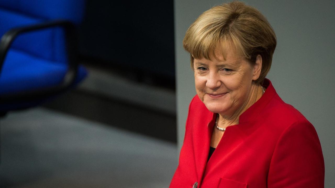 Merkel steht lächelnd im roten Kostüm am Rednerpult.