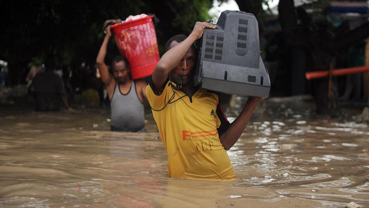 Menschen waten mit Fernsehern und Körben auf den Schultern durch die Fluten nach einer Überschwemmung in Somalia