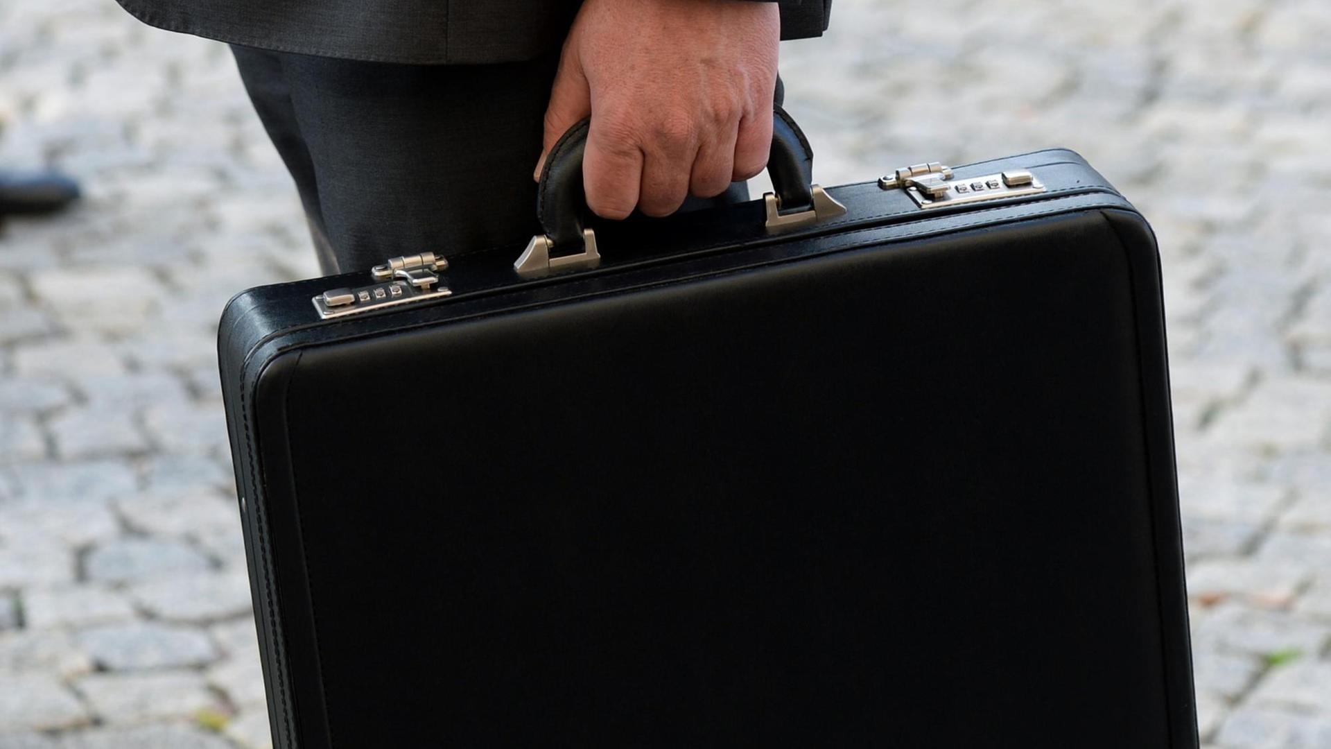 Ein Mann im schwarzen Anzug hält einen schwarzen Aktenkoffer mit Zahlenschloss.