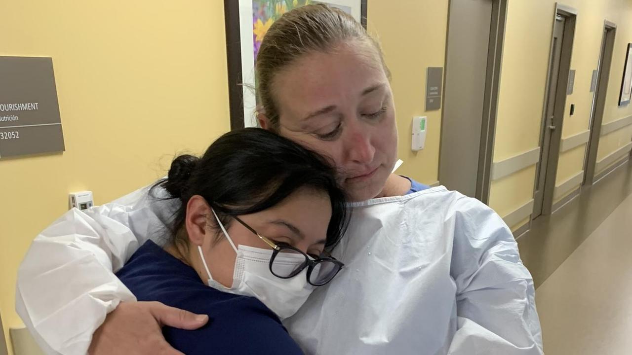 Zwei Krankenschwestern in Arbeitskleidung umarmen sich auf dem Gang eines Krankenhauses.