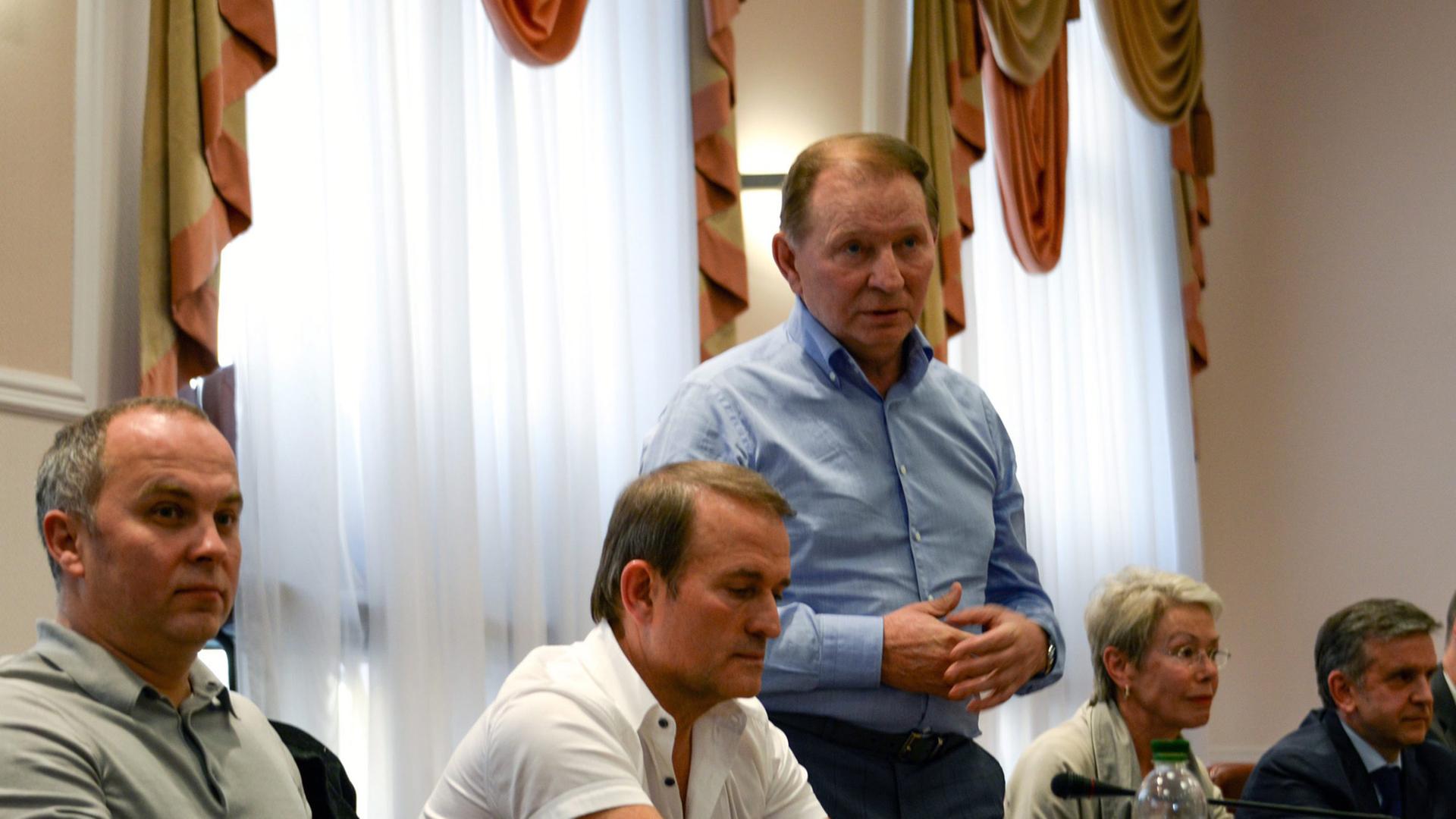 An einem Tisch sitzen Nestor Shufrich als Vertreter der ukrainischen Regierung, Viktor Medwedtschuk, eine Frau und ein Mann, in der Mitte zwischen ihnen steht Leonid Kutschma.