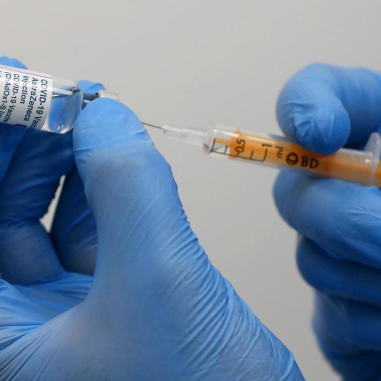 Zwei Hände in Handschuhen ziehen eine Spritze mit dem Astrazeneca-Impfstoff auf