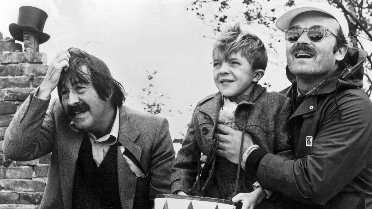 Auf einer schwarzweissen Aufnahme sind Günter Grass, David Bennent (als Blechtrommler Oskar Matzerath) und der Regisseur Volker Schlöndorff zu sehen.