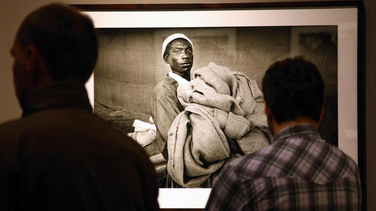 Zwei Menschen betrachten in einer Ausstellung in Berlin ein Bild des Fotografen Sebastião Salgado. Darauf zu sehen ist ein Mann mit Stoff in den Händen.