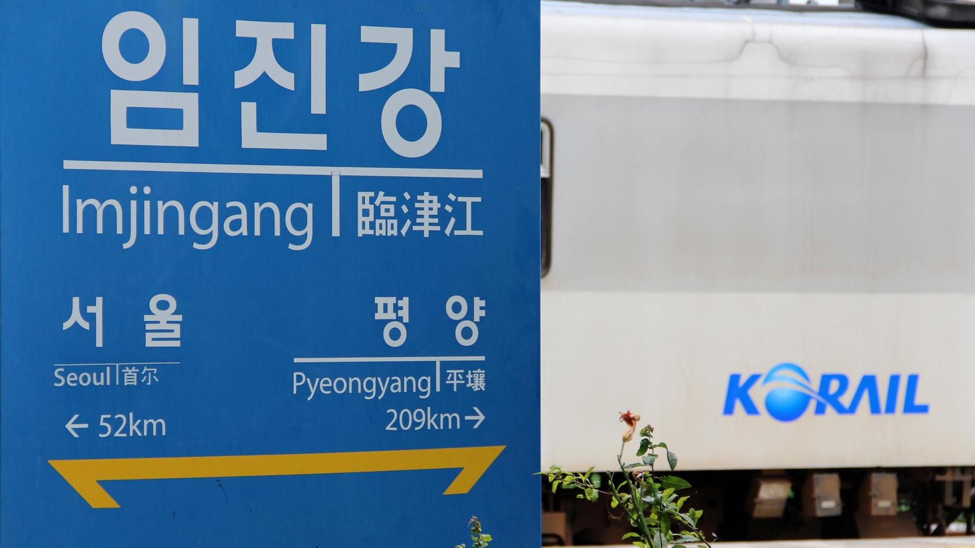 Schild an der koreanischen Grenze mit den Entfernungen zur südkoreanischen Hauptstadt Seoul und Pjöngjang in Nordkorea, dahinter ein Zug des südkoreanischen Eisenbahnunternehmens Korail.