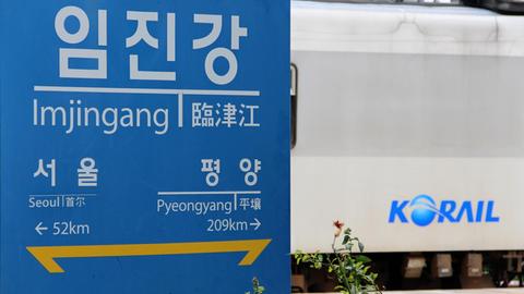 Schild an der koreanischen Grenze mit den Entfernungen zur südkoreanischen Hauptstadt Seoul und Pjöngjang in Nordkorea, dahinter ein Zug des südkoreanischen Eisenbahnunternehmens Korail.