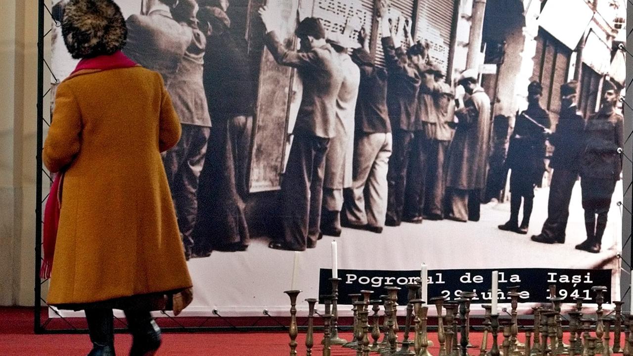 Eine ältere Frau steht vor einer übergroßen Schwarz-Weiß-Aufnahme in einer Holocaust-Ausstellung in Bukarest. Das Foto zeigt von rumänischen Sicherheitskräften umstellte Juden in Iasi im Jahr 1941.