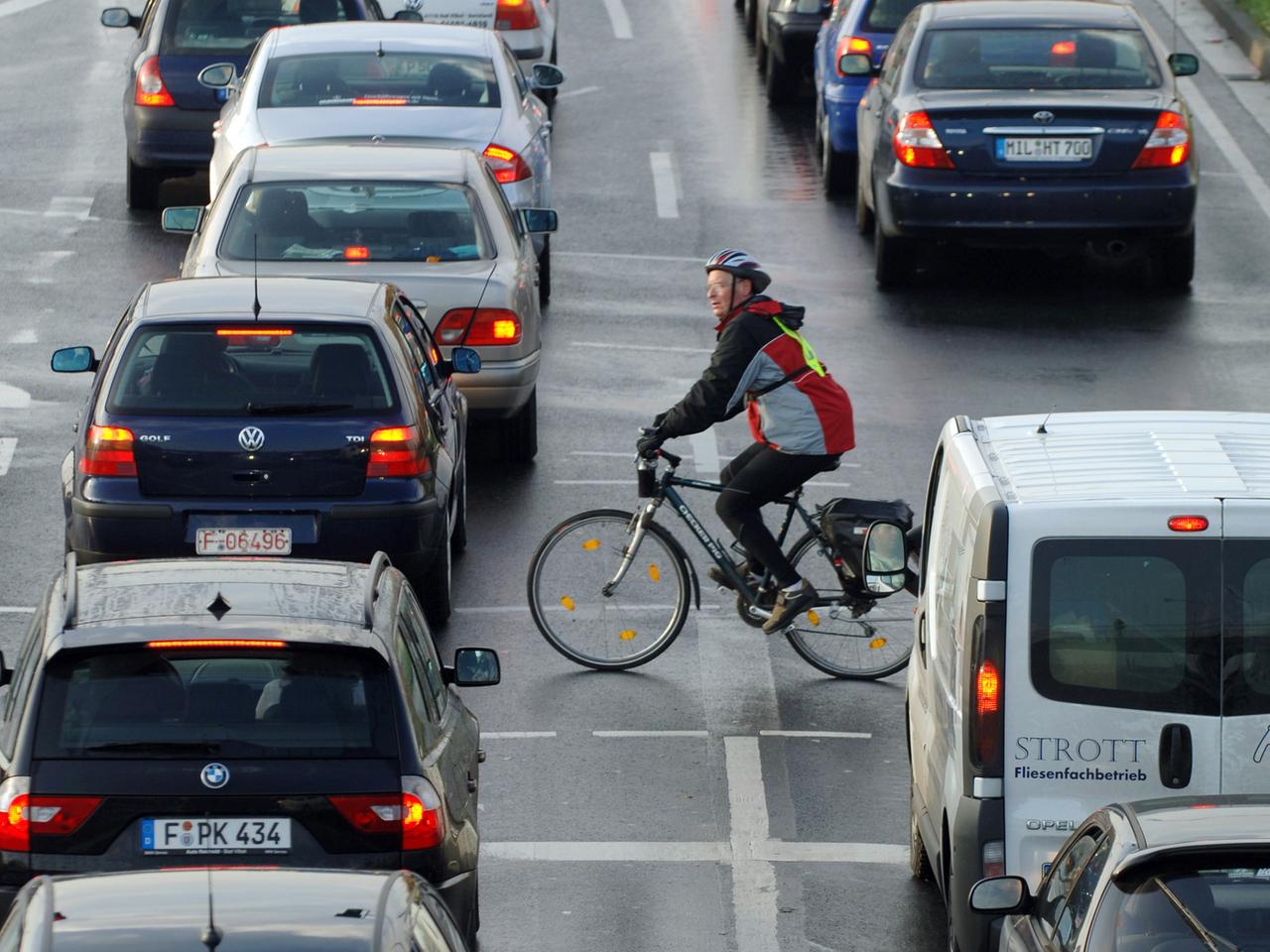 Ein Fahrradfahrer fährt zwischen Autos vorbei, die sich an einer Einfallstraße von Frankfurt am Main im Berufsverkehr stauen.