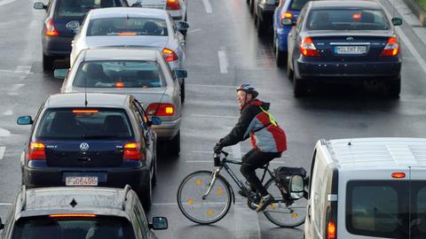 Ein Fahrradfahrer fährt zwischen Autos vorbei, die sich an einer Einfallstraße von Frankfurt am Main im Berufsverkehr stauen.