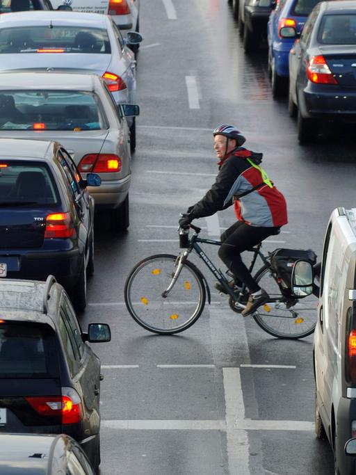 Ein Fahrradfahrer fährt zwischen Autos vorbei, die sich an einer Einfallstraße von Frankfurt am Main im Berufsverkehr stauen.
