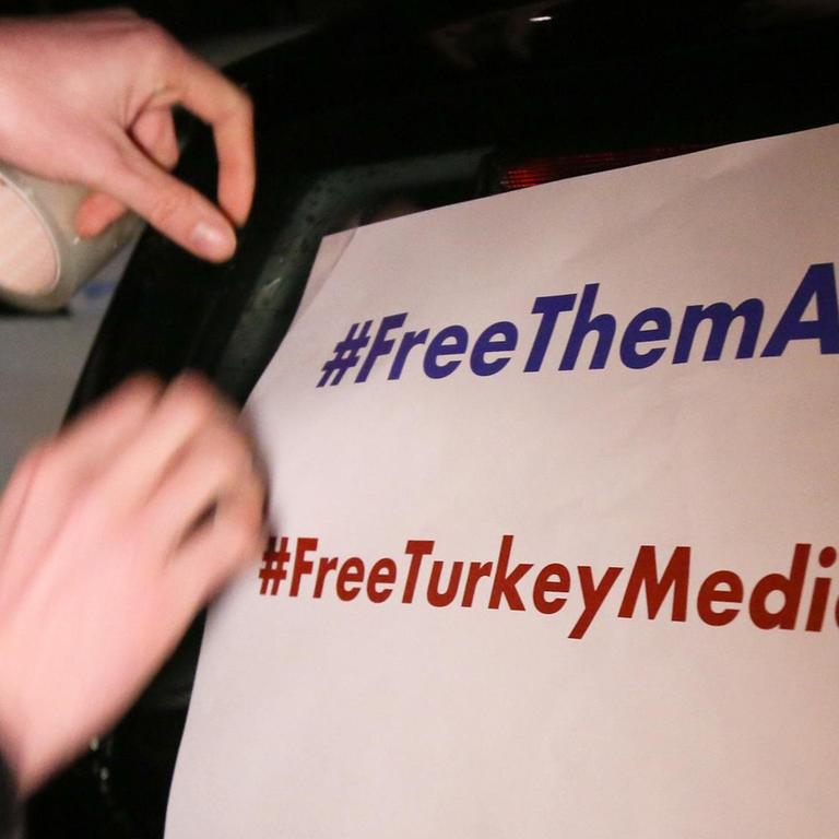 Ein Mann klebt ein Plakat mit der Aufschrift "#FreeThemAll" und "FreeTurkeyMedia" vor dem Start eines Autokorsos für den "Welt"-Korrespondenten Deniz Yücel an einen Pkw. 