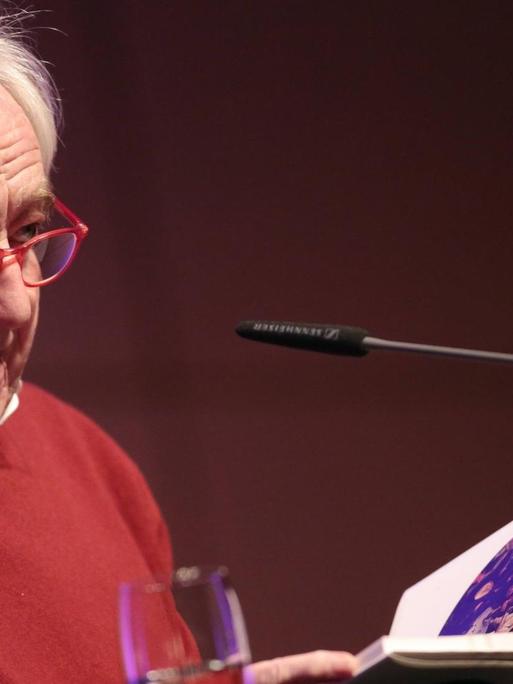 Der niederländische Schriftsteller Cees Noteboom sitzt bei der lit.Cologne 2016 hinter einem Tisch und liest aus einem Buch.