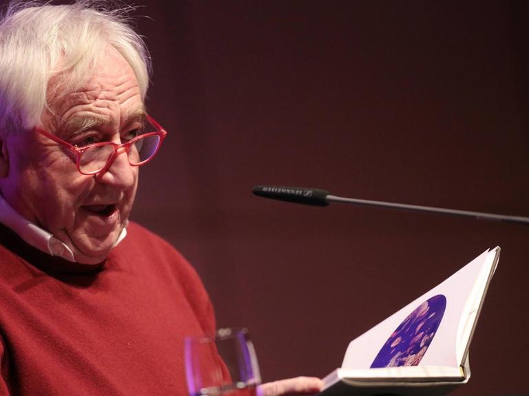 Der niederländische Schriftsteller Cees Noteboom sitzt bei der lit.Cologne 2016 hinter einem Tisch und liest aus einem Buch.