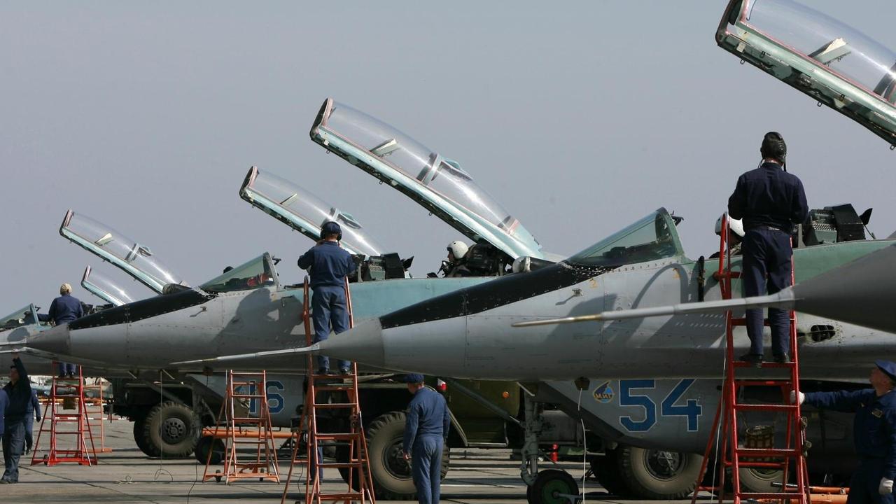 Die Kampfjets werden von Technikern gewartet, die auf roten Leitern an den Cockpits stehen. Darin sitzen Piloten mit Helmen. Die Glasklappen der Cockpits sind geöffnet.