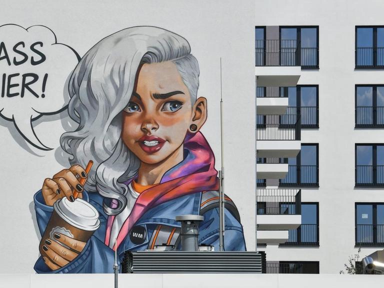 Graffiti auf einer Hauswand, das ein Mädchen zeigt mit der Sprechblase "Krass hier!"